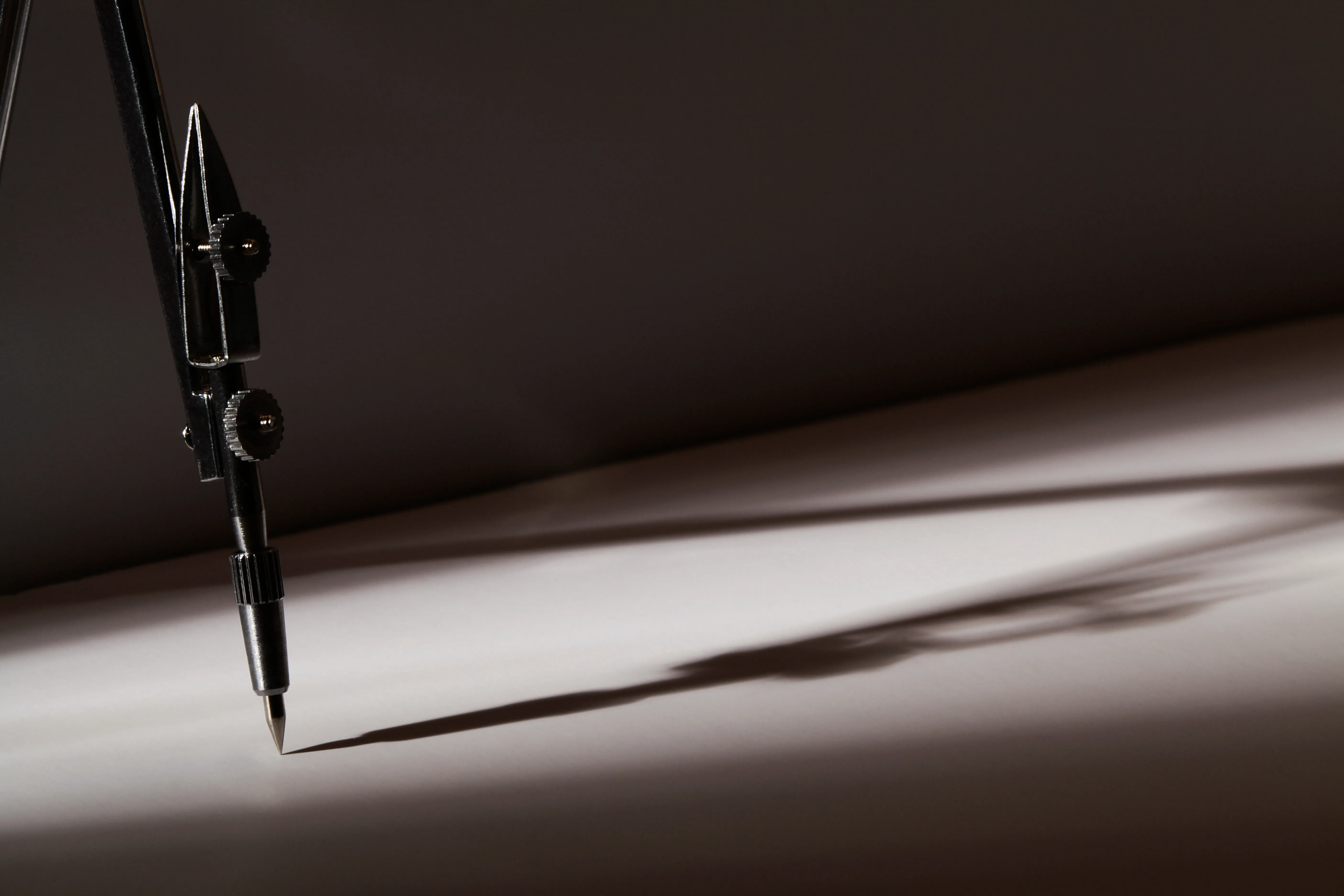 A precision compass casting intersecting geometric shadows across paper